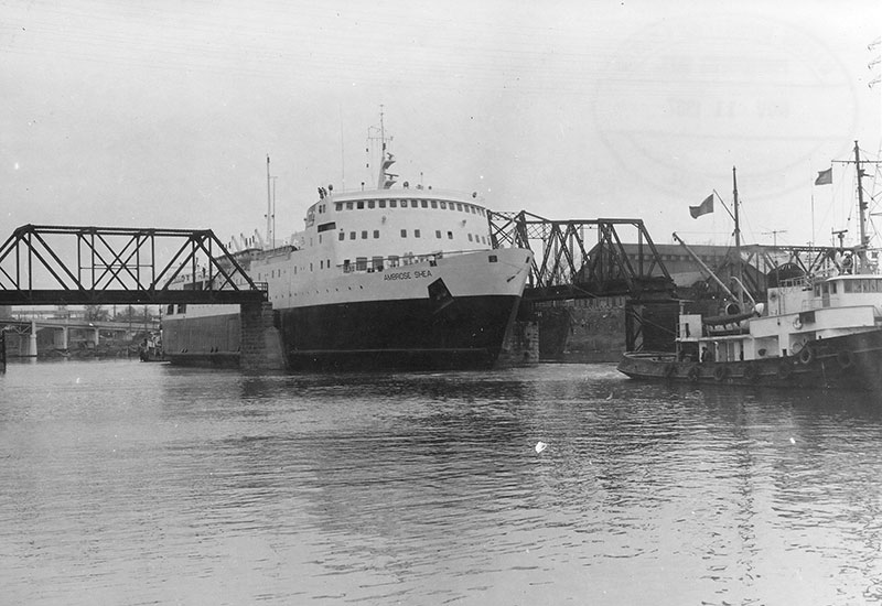 Le traversier <em>Ambrose Shea</em> naviguant sur la rivière Richelieu entre les piliers du pont de la voie ferrée. 