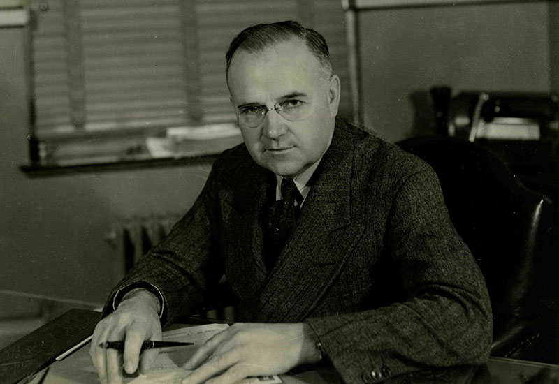 Ludger Simard portant des lunettes assis à son bureau